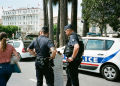 Police officers and a civilian interact near a police car on a busy city street.